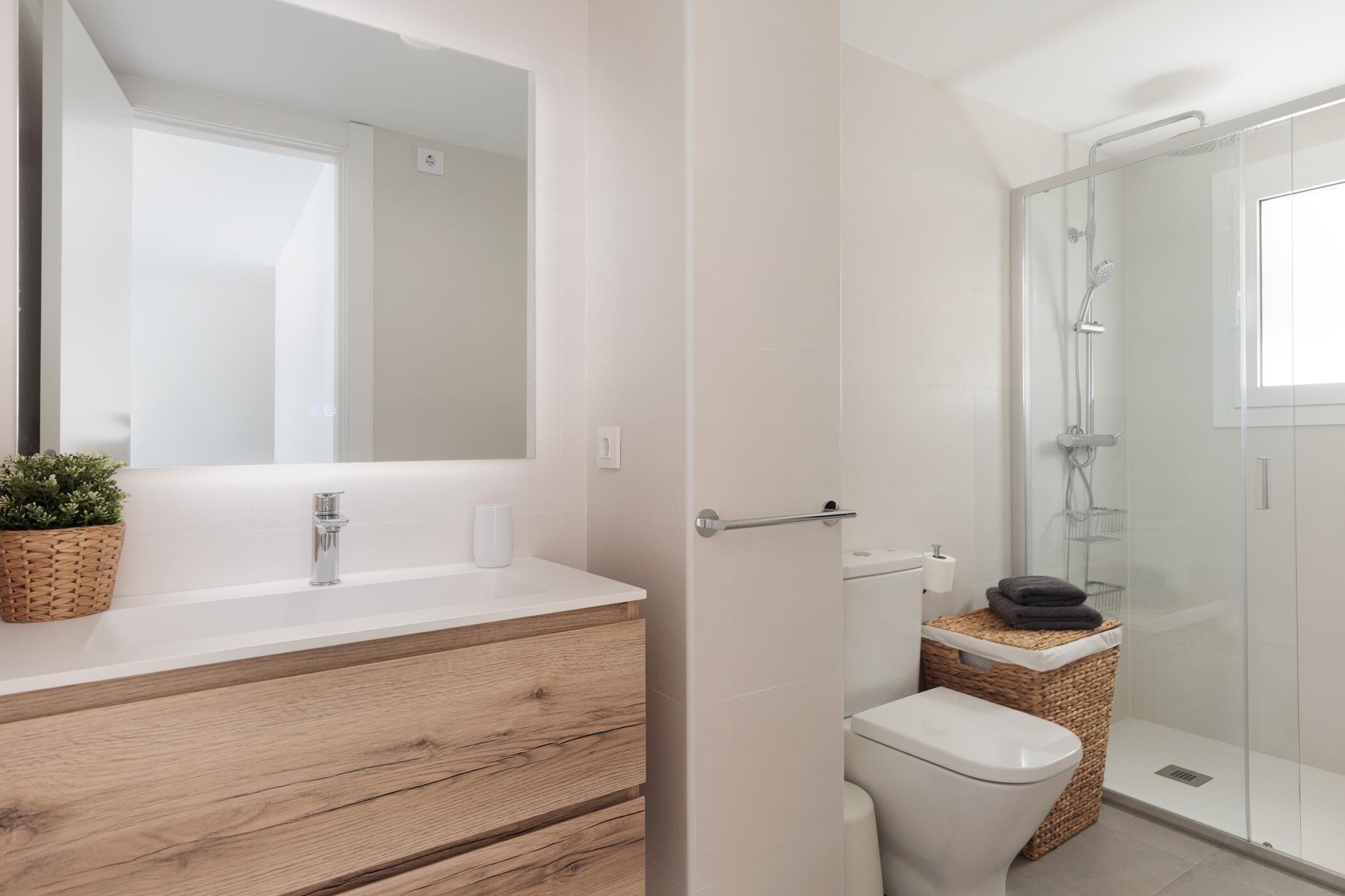 A modern bathroom with a wooden vanity, a glass shower enclosure, and a large mirror.