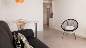A modern living room with a sofa, a dining table, a black chair, and a hanging light fixture.