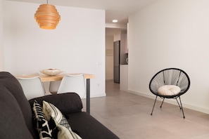 A modern living room with a sofa, a dining table, a black chair, and a hanging light fixture. - WHITE APARTMENT with TERRACE, AC & PARKING, NEAR BEACH (Tossa de Mar)