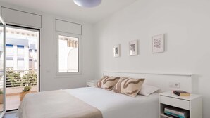 A bedroom with a bed, a bedside table with books, a window, and a view of a building outside.