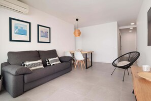 A modern living room with a grey sofa, a dining table with chairs, a black chair, and two framed pictures on the wall. - WHITE APARTMENT with TERRACE, AC & PARKING, NEAR BEACH (Tossa de Mar)