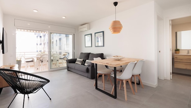 A modern living room with a dining area, a sofa, a coffee table, and a hanging light fixture.