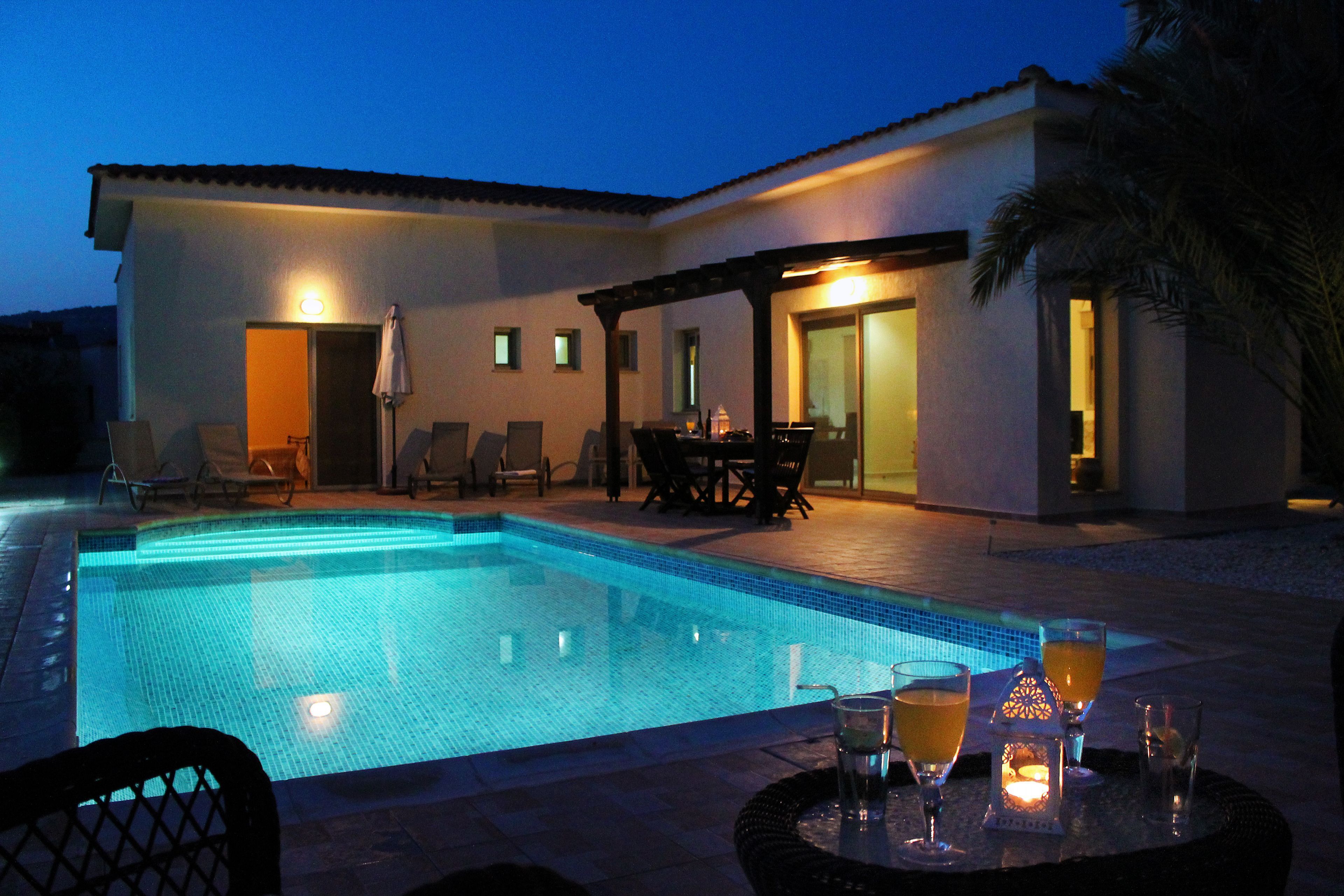 A swimming pool with lounge chairs and a table with drinks, surrounded by a building with doors and windows.