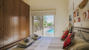 A bedroom with a bed, a wooden wardrobe, a view of an outdoor swimming pool, and a ceiling fan. - 'The Winning Post' - 3 Bed, 2 Bath, Single Storey Villa with Private Pool in Sea Caves (Peyia)