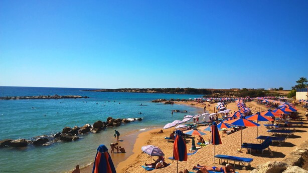 A beach with umbrellas and sun loungers, rocky shoreline, and clear blue water. - 'The Winning Post' - 3 Bed, 2 Bath, Single Storey Villa with Private Pool in Sea Caves (Peyia)