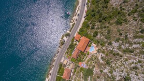 Vista aérea de una propiedad costera con piscina, camino y ladera rocosa.