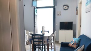 A living room with a blue sofa, a television, and a dining area with a table and chairs. - Villa Fascinosa with sea / island currents view (portopalo di capo passero)