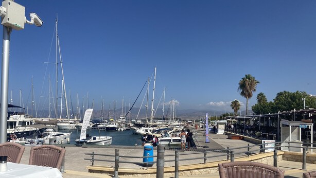 Un port de plaisance avec des bateaux amarrés, un ciel dégagé et des tables et des chaises disposées à l’extérieur pour permettre aux clients de s’asseoir.