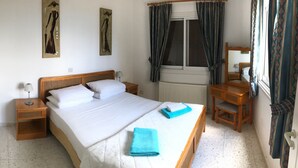 Une chambre à coucher comprenant un lit, des tables de chevet, une commode, une coiffeuse, une fenêtre avec des rideaux et un radiateur.