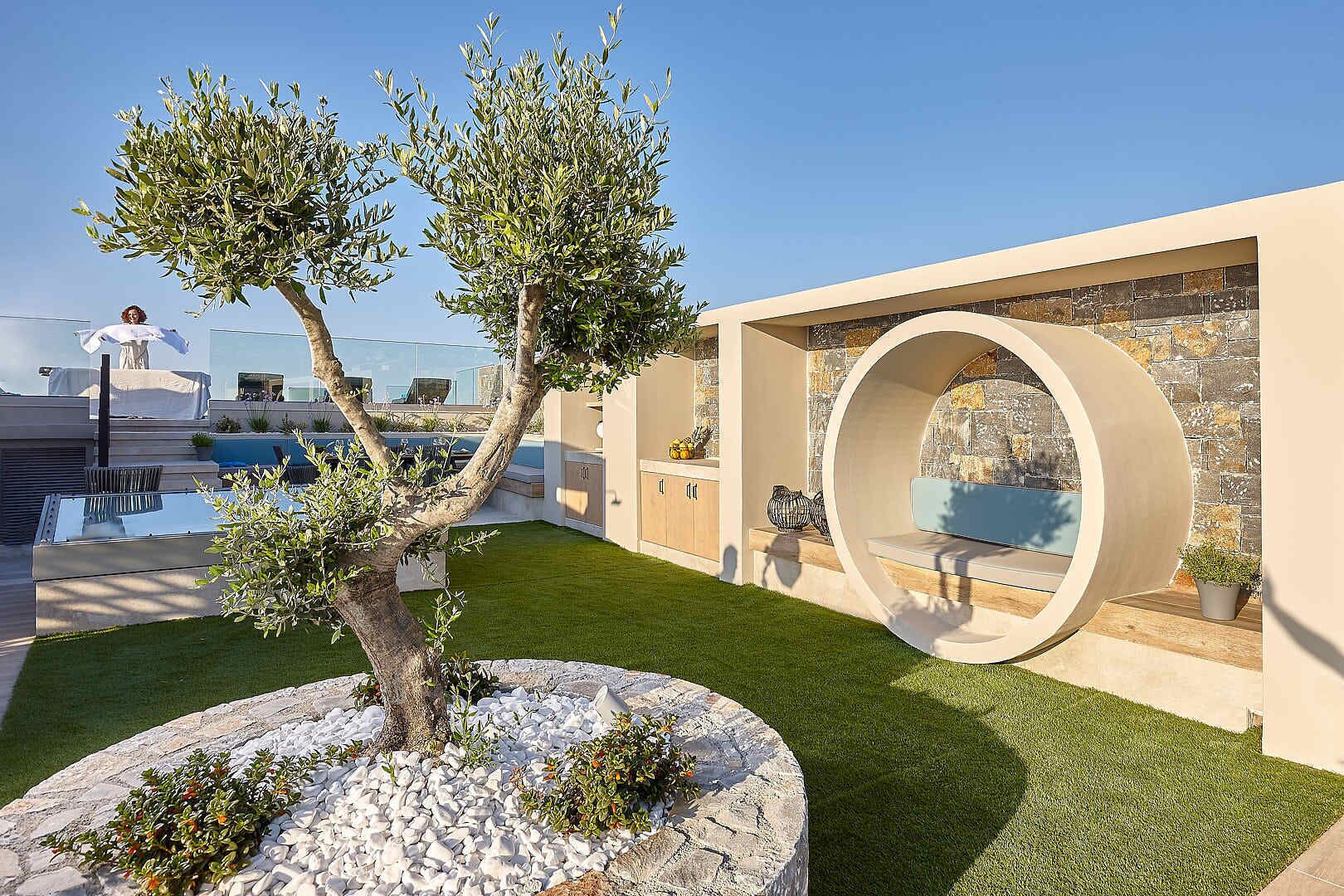 A modern outdoor area with a pool, a circular seating structure, and a well-maintained lawn.