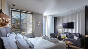 Moderni hotellihuone, jossa on suuri sänky, sohva, televisio ja ikkuna, jossa on sälekaihtimet.