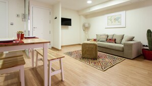 Een moderne woonkamer met een houten eettafel, een bank, een klein poufje en een cactus.