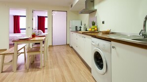 Een compacte keuken met een wasmachine, een eethoek met tafel en stoelen, en een bed in de aangrenzende kamer.