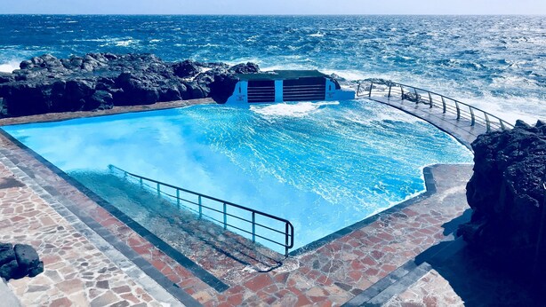 Una piscina con vista sull'oceano, circondata da piastrelle di pietra e una ringhiera metallica.