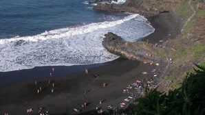 Una zona costiera con un litorale roccioso, una spiaggia con persone che prendono il sole e un sentiero che sale sulla scogliera.
