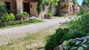 Un edificio rústico de piedra con camino de grava y exuberante vegetación.