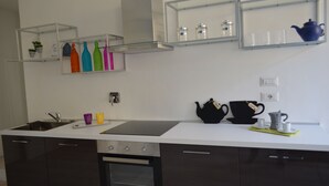 A modern kitchen with a white countertop, stainless steel appliances, and glass shelves with colorful bottles and kitchenware. - Apartment in the historic center of Perugia (Perugia)