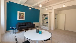 A modern living room with a blue accent wall, a black sofa, a white dining table with four chairs, and a white cabinet with shelves. - Apartment in the historic center of Perugia (Perugia)