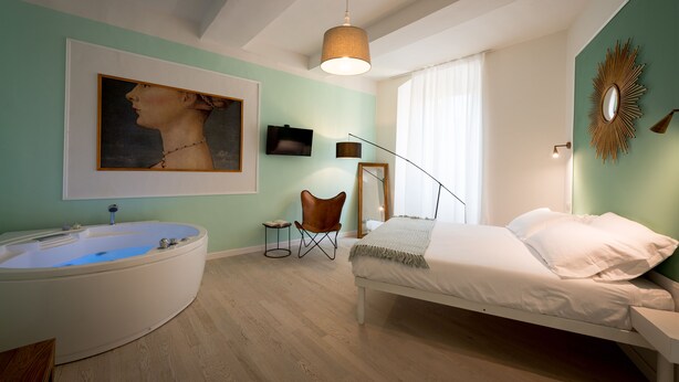 A bedroom with a large bathtub, a bed, a chair, and a painting on the wall. - Apartment in the historic center of Perugia (Perugia)