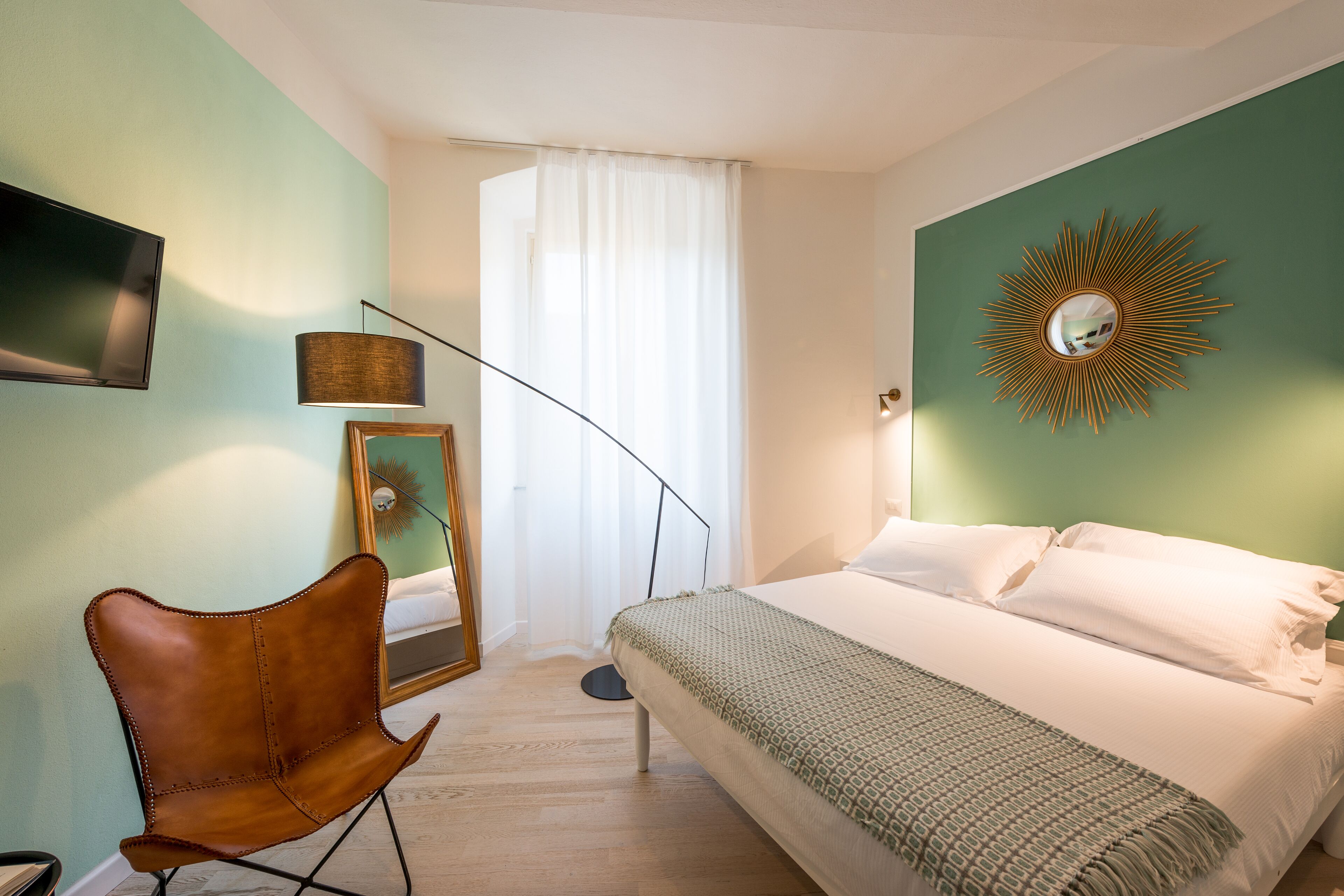 Ein Schlafzimmer mit einem Bett, einem Sessel, einem Spiegel und einem Fernseher an der Wand.
