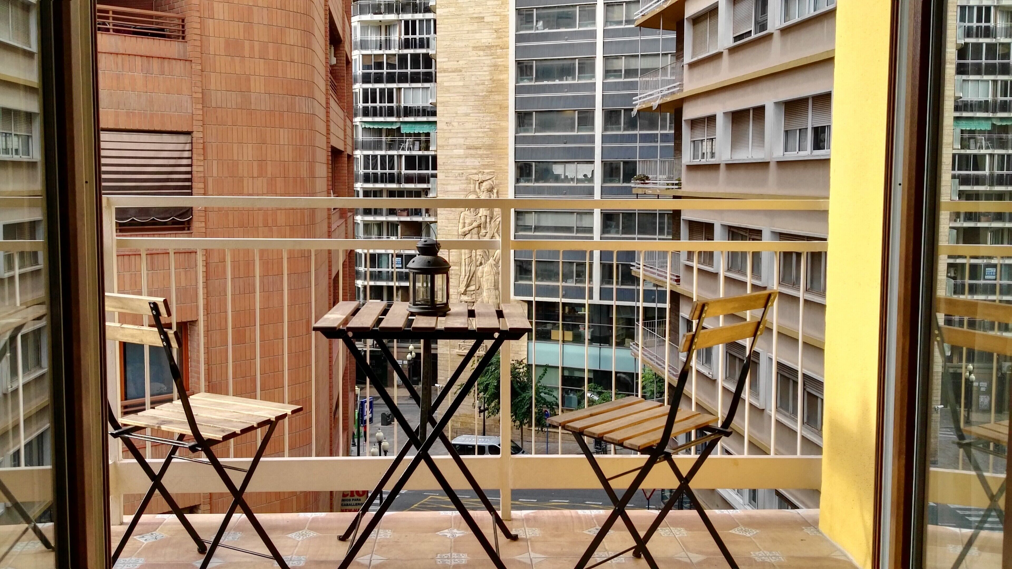 Een balkon met een kleine tafel en twee stoelen, met uitzicht op een stadsgezicht met wolkenkrabbers.