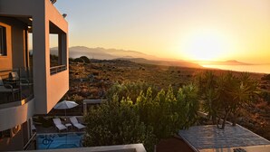 A modern building with a pool, lounge chairs, and a view of the sunset over a desert landscape. - Unique Sea View,Sunset with Privacy! Bedrooms with ensuite bathroom,Jacuzzi,GYM (Rethymno)