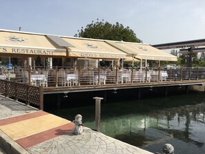 A waterfront restaurant with outdoor seating and a dock extending over the water. - Apartment in Kings Palace with a sunset view and an easy walk to Venus Beach (Paphos)