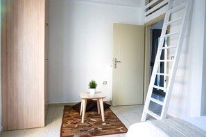 A room with a wooden wardrobe, a small table with a potted plant, a white door, and a white ladder leaning against the wall.