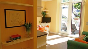Een woonkamer met een eetgedeelte, een televisie en een schuifdeur naar een terras.