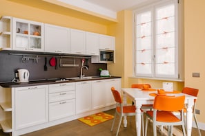 Een moderne keuken met witte kastjes, een magnetron en een eethoek met oranje stoelen.