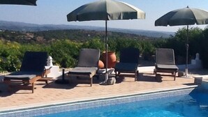 Zona junto a la piscina con sillones de descanso y sombrillas, con vista a un paisaje montañoso.