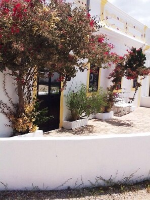 A courtyard with white walls, potted plants, and a seating area with tables and chairs. - Stunningly Restored Farmhouse With Private Pool, Panoramic Views & Large Garden (Barranco De Sao Miguel, Azinheiro)