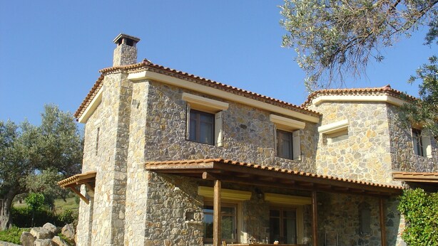 Una casa de piedra con techo de tejas, un porche cubierto y un jardín.
