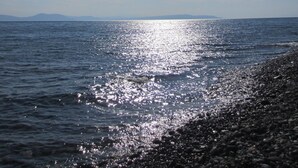Una playa con costa rocosa y agua tranquila que refleja el sol.