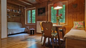 Interior acogedor de una cabaña con piso de madera, un sofá, una mesa de comedor con sillas y una ventana con vista a follaje.