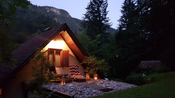 Una cabaña acogedora con techo inclinado, puerta de madera y un pequeño porche con una silla y una mesa.