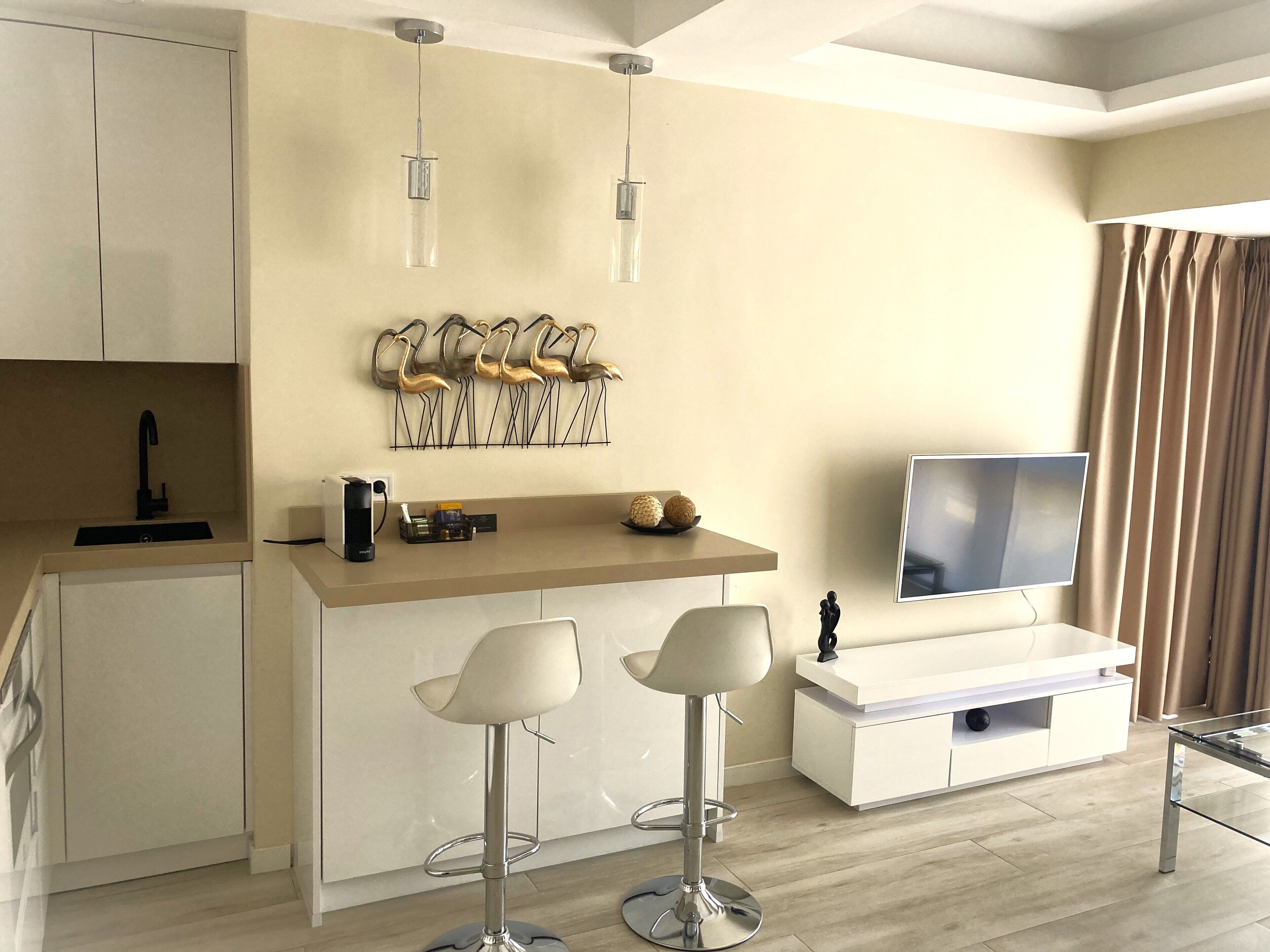 Una cocina moderna con una isla central, taburetes de bar, un televisor de pantalla plana y un elemento decorativo en la pared.
