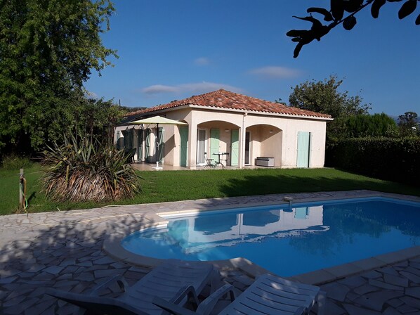Una casa con piscina, un patio con sillones de descanso y un jardín.