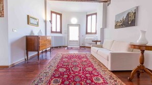 Un vaste salon agrémenté d’un grand tapis rouge à motifs, d’un canapé blanc, d’un meuble en bois et d’un tableau accroché au mur.