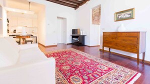 Un salon avec un canapé blanc, un tapis rouge à motifs, un meuble en bois et un téléviseur.