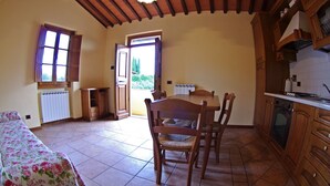 Une cuisine avec des meubles en bois, une table à manger avec des chaises, un radiateur et un lit avec une literie à motifs floraux.