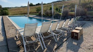 A swimming pool with lounge chairs and umbrellas, surrounded by a stone deck and a natural landscape.