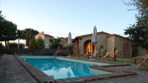 A swimming pool with a brick deck, lounge chairs, and umbrellas.