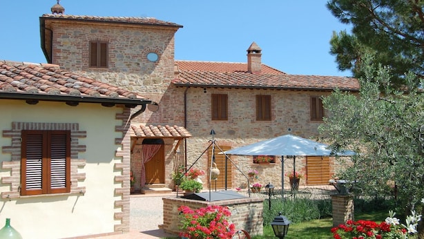 A traditional stone building with a tiled roof, a small tower, and a courtyard with potted plants and outdoor furniture.