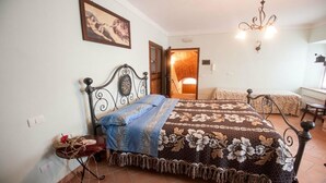 A bedroom with a bed, a chair, a table, and a door leading to another room.