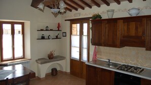 A kitchen with wooden cabinets, a gas stove, a sink, and a window with a view of the outside.