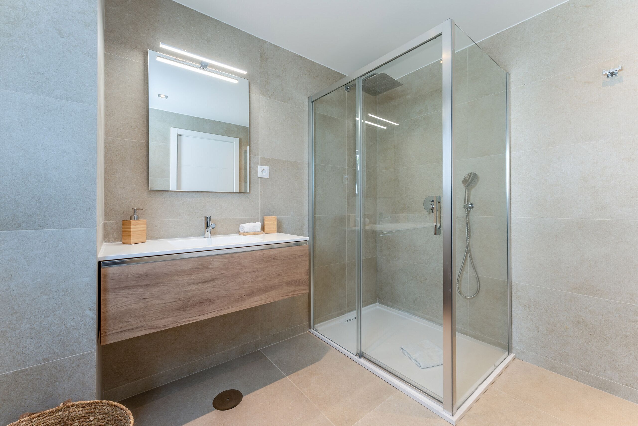 A modern bathroom with a glass-enclosed shower, a wooden vanity, and a large mirror.