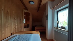 Una habitación de cabaña de madera con una cama, un ventanal con cortinas y una puerta con paneles de vidrio.