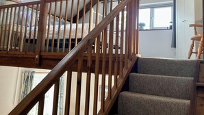A wooden staircase with a loft bedroom above, carpeted steps, and a skylight.