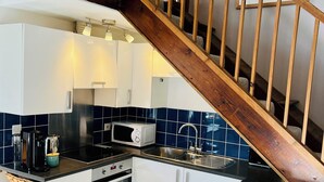 A modern kitchen with white cabinets, a black countertop, a wooden staircase, and a blue tiled backsplash.